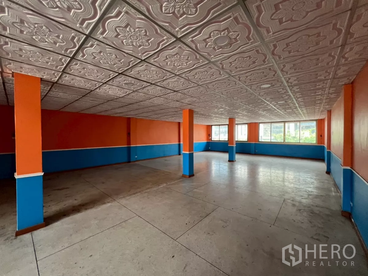Shophouse for rent in Watthana, Bangkok - Wide open floor with patterned ceiling, orange and blue walls, and ample natural light.