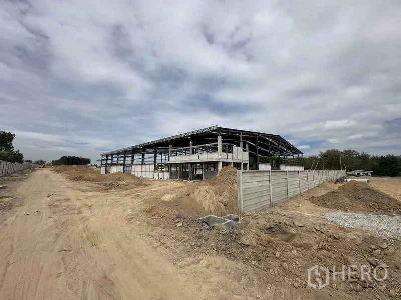 Warehouse for rent or sale in Nikhom Phatthana, Rayong - Exterior corner of the warehouse shell with boundary fencing and site access road.