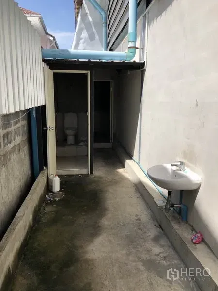 Warehouse for rent in Mueang Samut Prakan, Samut Prakan - External restroom block with toilets and a wall-mounted sink along a service alley.