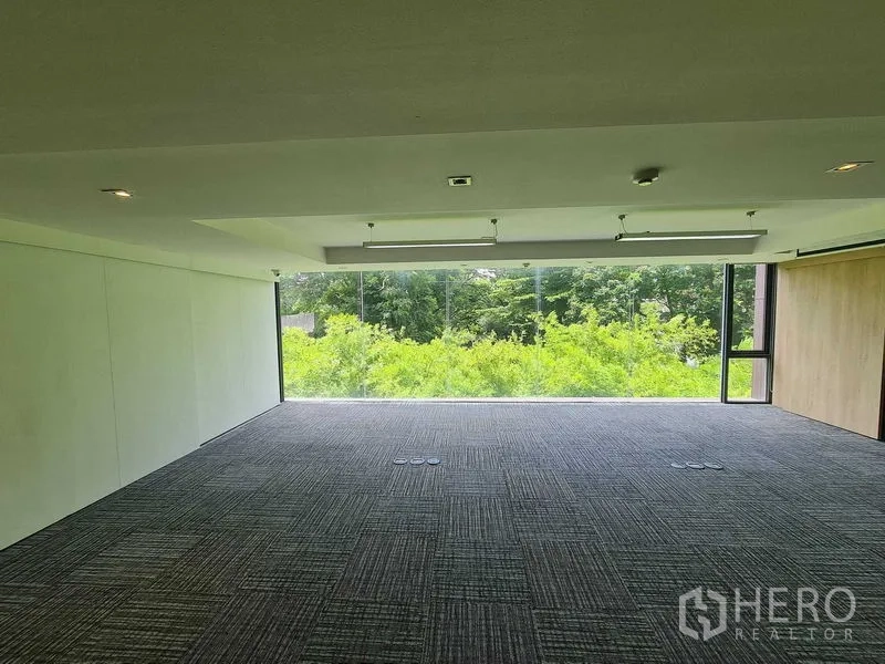 Office Space for rent in Watthana, Bangkok - Spacious office floor with panoramic glass overlooking trees, dark carpet tiles, floor outlet boxes and ceiling LED fixtures.