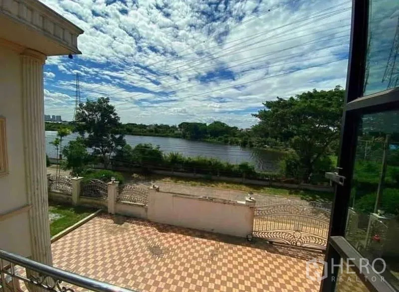 Detached House for sale in Prawet, Bangkok - Balcony view over the tiled courtyard toward a lakeside lined with trees.