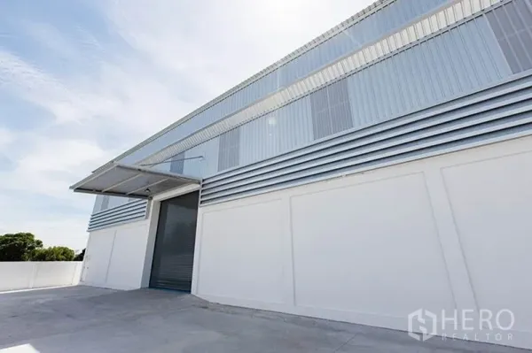 Factory for rent in Bang Phli, Samut Prakan - Side view of the warehouse facade with metal cladding, high roof, and covered loading bay roller door.