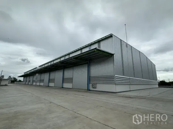 Warehouse for rent in Wang Noi, Phra Nakhon Si Ayutthaya - Large modern steel warehouse with wide loading canopies and an expansive concrete yard under a cloudy sky in Wang Noi.