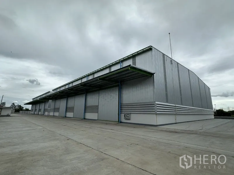 Warehouse for rent in Wang Noi, Phra Nakhon Si Ayutthaya - Large modern steel warehouse with wide loading canopies and an expansive concrete yard under a cloudy sky in Wang Noi.