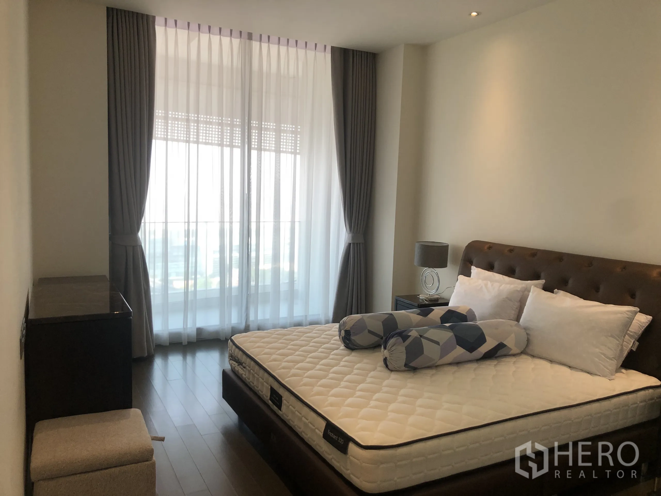 Condominium for rent in Pathum Wan, Bangkok - Sunlit bedroom with upholstered bed, large windows with sheer drapes and warm lighting.