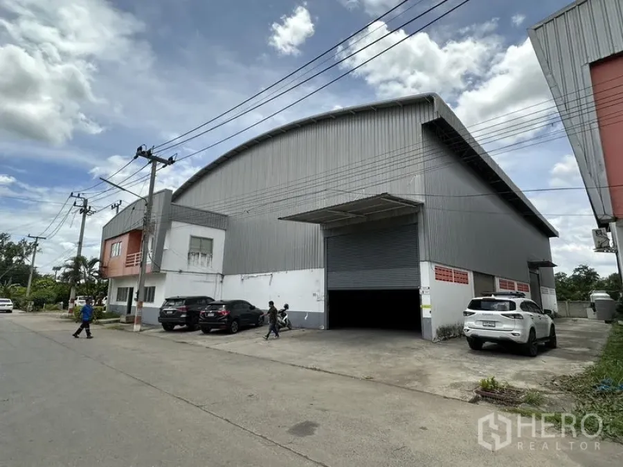 Factory for rent in Phra Nakhon Si Ayutthaya - Street view of a large steel-clad factory with curved roof, wide roller shutter and front parking.