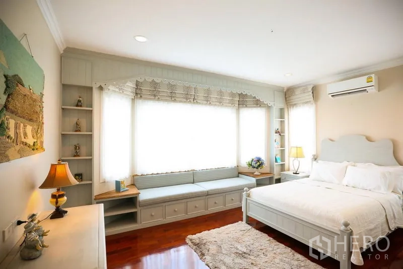 Detached House for rent in Bang Na, Bangkok - Sunlit guest bedroom with big window seat, built-in shelves and white bed frame.