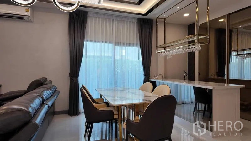 独立式住宅 出租或出售在Bang Na, Bangkok - 餐区配大理石餐桌与悬挂酒杯架，窗帘柔和。