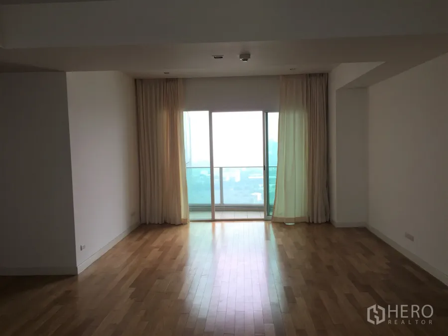 Condominium for rent in Khlong Toei, Bangkok - Spacious living room with hardwood floors, sheer curtains and a sliding door opening to a balcony with Bangkok skyline views.