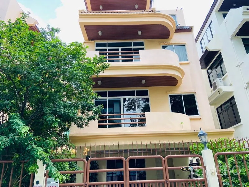 Detached House for rent in Watthana, Bangkok - Three-storey beige detached house with curved balconies, large windows and a gated frontage.