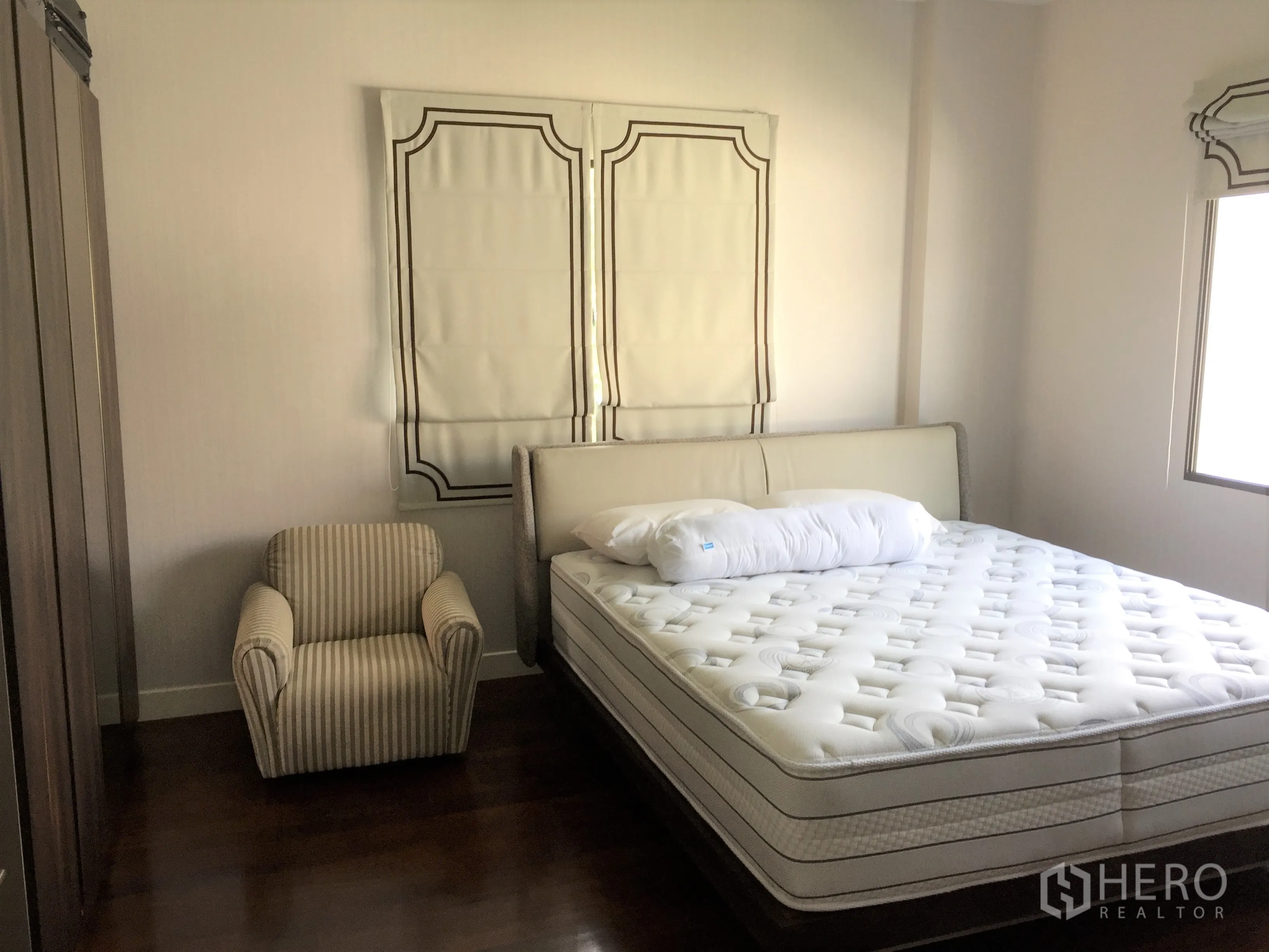 Detached House for rent or sale in Prawet, Bangkok - Guest bedroom with upholstered bed, striped armchair, wardrobe and soft natural light.