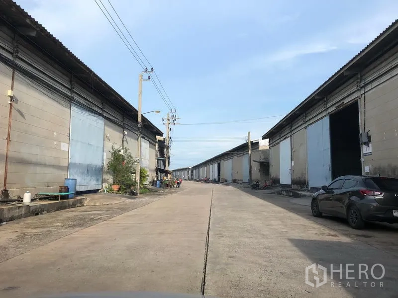 Warehouse for rent in Bang Phli, Samut Prakan - Industrial estate roadway lined with warehouse units and wide truck access.