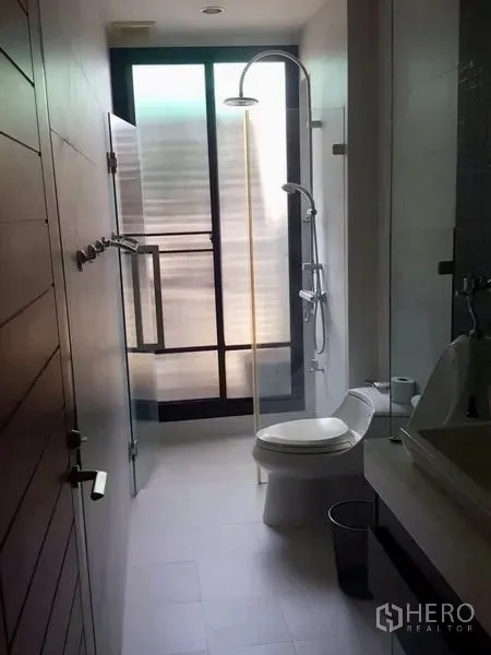 Home Office for rent or sale in Bang Rak, Bangkok - Slim bathroom with glass shower, rain head, toilet and a frosted window.