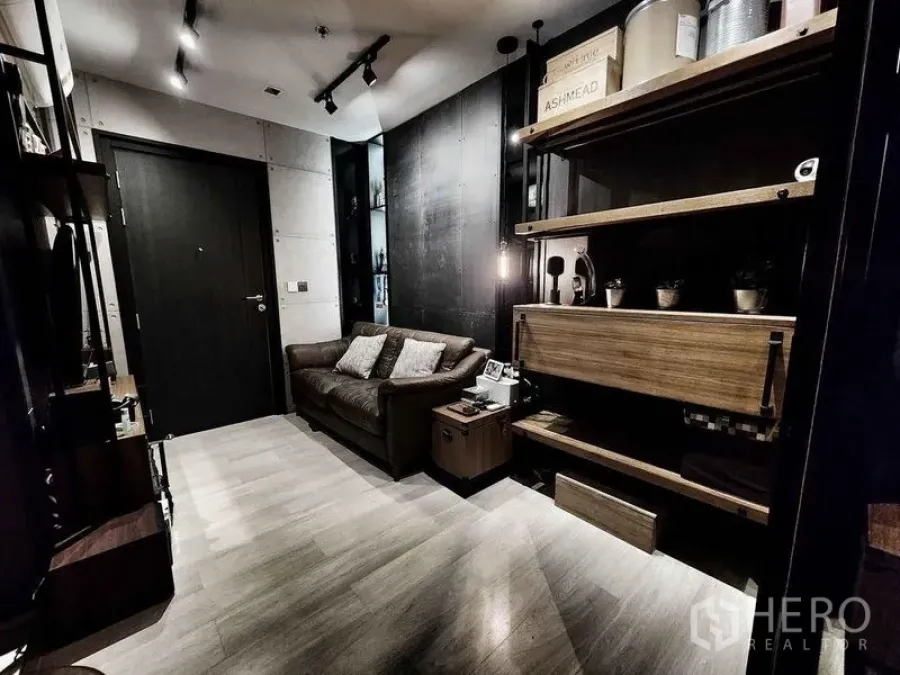 Condominium for sale in Pathum Wan, Bangkok - Wide view of living room with entrance door, shelving wall, and leather sofa.