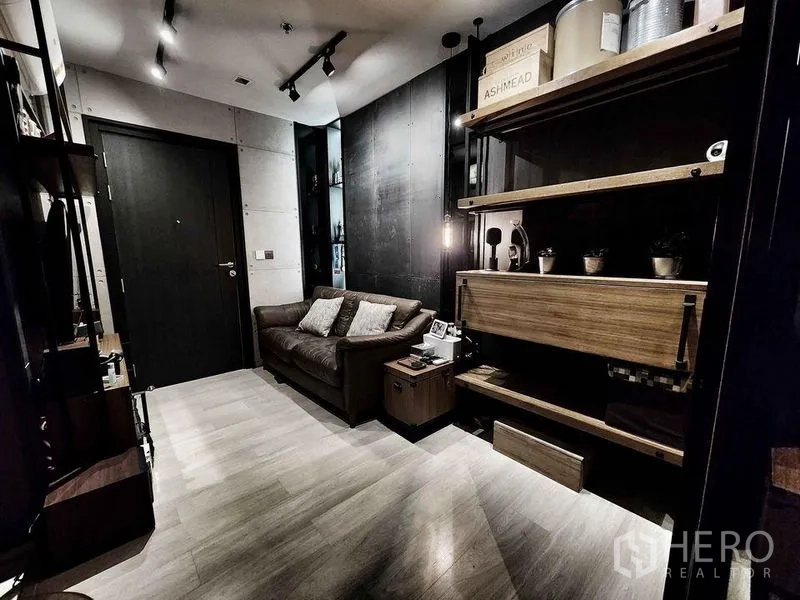 Condominium for sale in Pathum Wan, Bangkok - Wide view of living room with entrance door, shelving wall, and leather sofa.