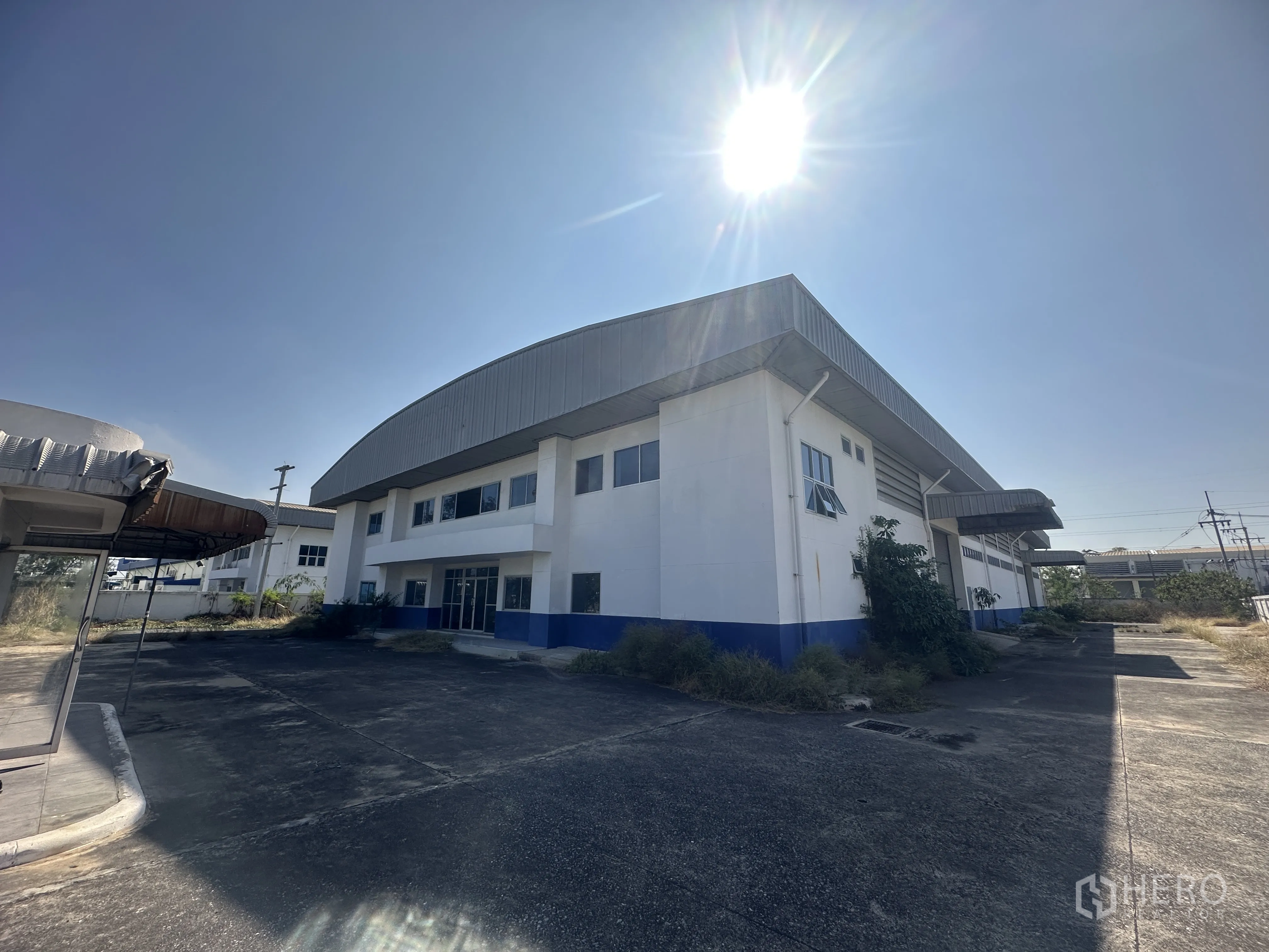 Factory for rent in Bang Pa-in, Phra Nakhon Si Ayutthaya - Exterior view of the factory building with metal roof and large paved driveway under clear sky.