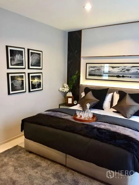 Condominium for rent in Khlong Toei, Bangkok - Master bedroom with plush bedding, bedside decor and framed artwork.