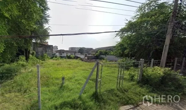 Land for rent in Khlong Toei, Bangkok - Grassy, level land with a simple metal gate, power lines above and low-rise homes nearby.