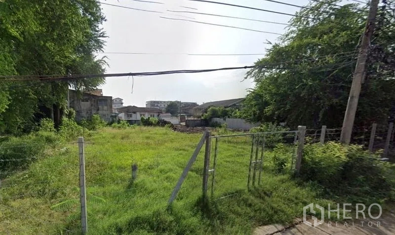 Land for rent in Khlong Toei, Bangkok - Grassy, level land with a simple metal gate, power lines above and low-rise homes nearby.