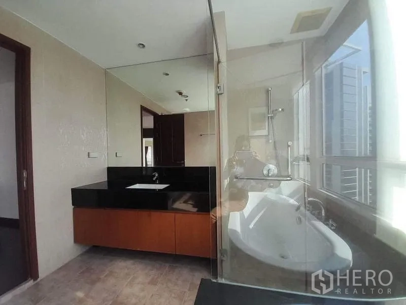 Condominium for rent or sale in Pathum Wan, Bangkok - Bright bathroom featuring a glass shower, soaking tub, and black stone vanity counter.
