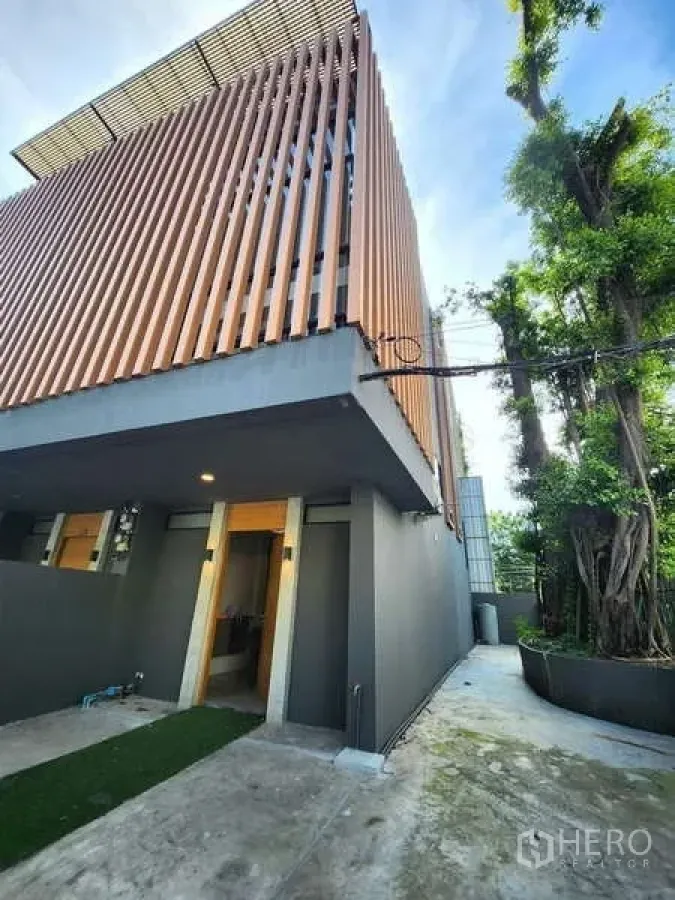 Townhouse for rent in Watthana, Bangkok - Modern townhouse exterior with vertical timber screens, gray facade, and a private driveway.