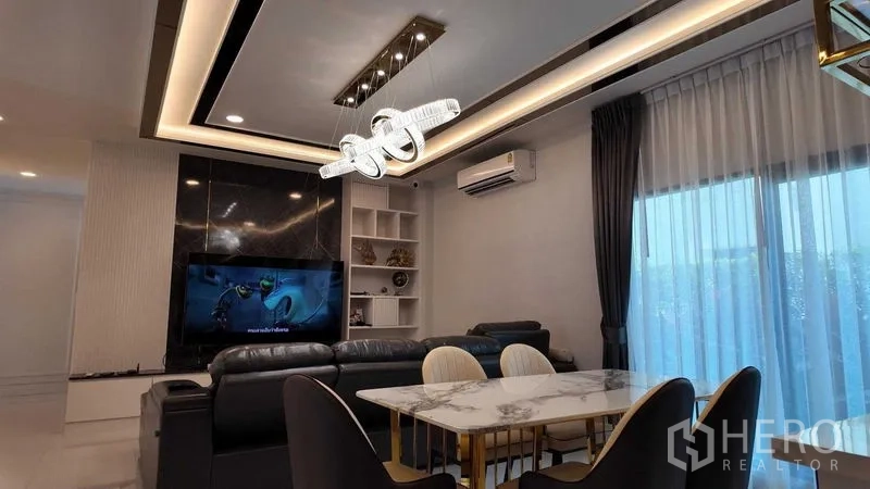 独立式住宅 出租或出售在Bang Na, Bangkok - 客厅配沙发与电视墙，现代吊灯并连通餐区。
