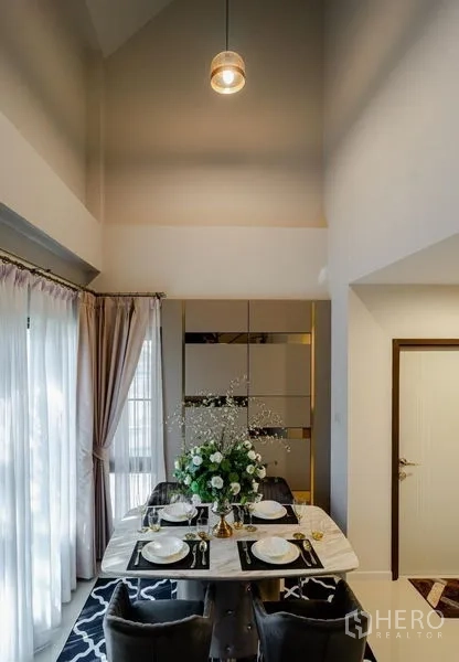 Detached House for sale in Lam Luk Ka, Pathum Thani - Double-height dining area with marble table and tall curtains.
