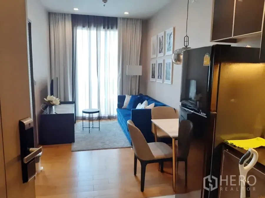 Condominium for rent in Khlong Toei, Bangkok - Bright living room with a blue sofa, TV console and floor-to-ceiling curtains.