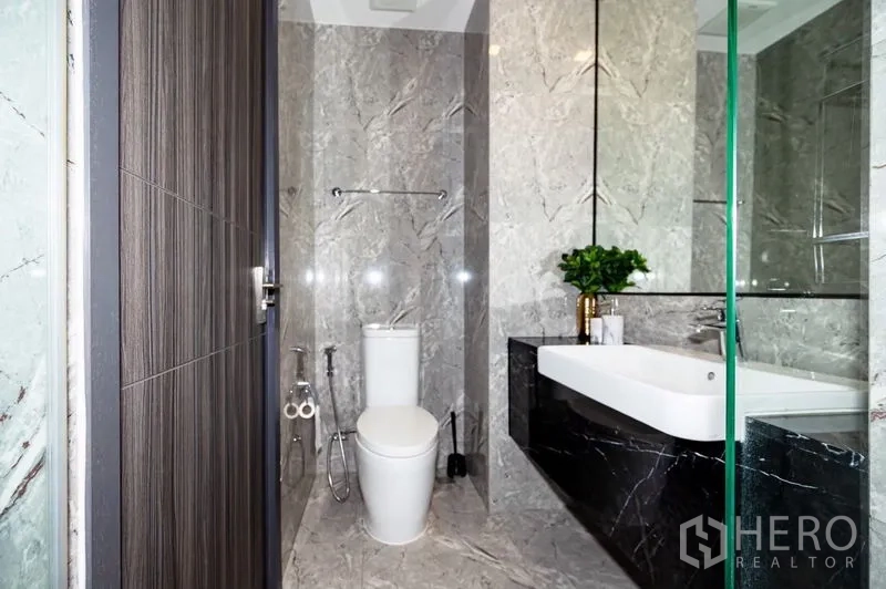 Condominium for rent in Watthana, Bangkok - Contemporary bathroom with gray marble tiles, glass shower enclosure, and white vanity.