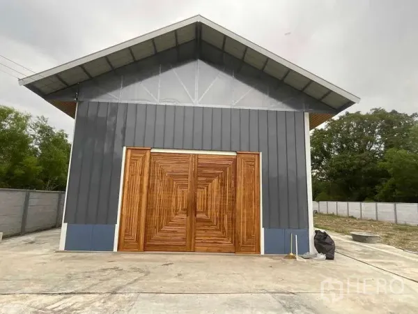 Warehouse for rent or sale in Nong Chok, Bangkok - Warehouse facade with pitched roof, dark metal siding and large timber double doors.