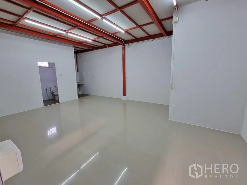 Warehouse for rent in Lam Luk Ka, Pathum Thani - Ground-floor office area with glossy tiles, visible pantry and restroom doorway.