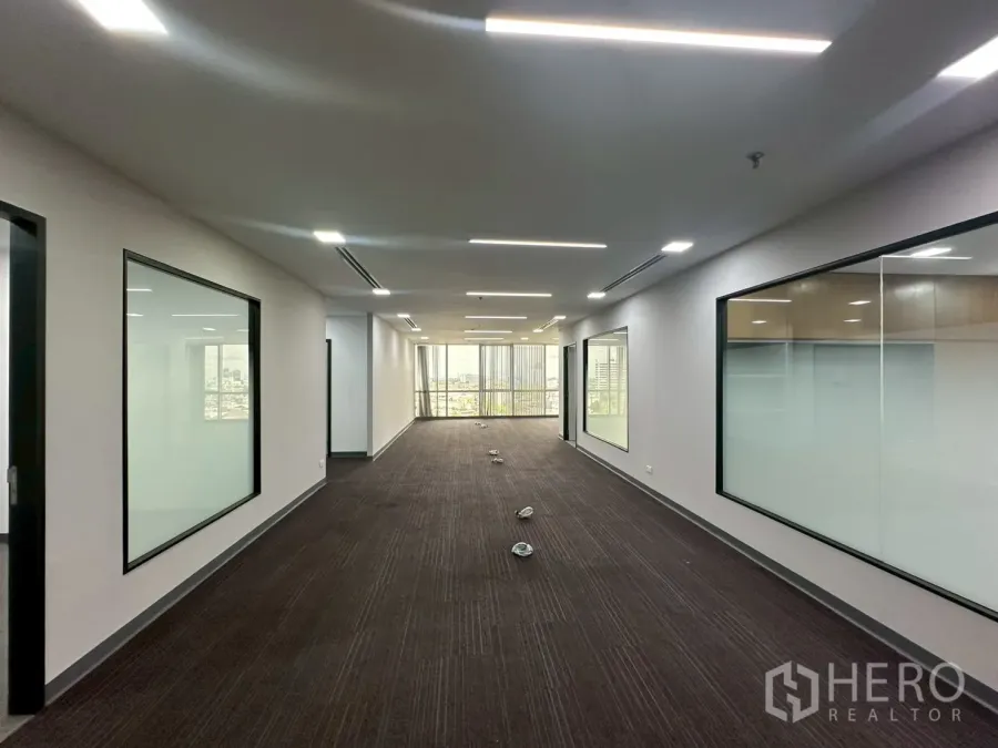 Office Space for rent - Long open-plan corridor with carpet flooring, glass-partitioned rooms and LED lights.