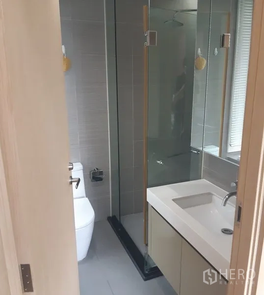 Condominium for rent in Khlong Toei, Bangkok - Second bathroom with vanity, mirror and a walk-in glass shower.
