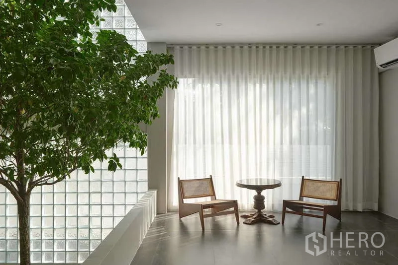 Home Office for sale in Chatuchak, Bangkok - Quiet sitting corner with two woven chairs, round table, glass‑block wall and indoor tree.
