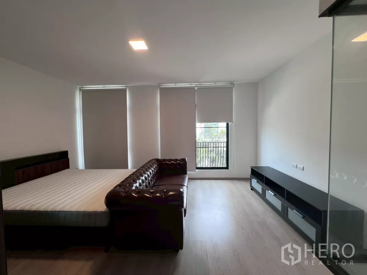 Townhouse for rent in Bang Phli, Samut Prakan - Spacious master bedroom with king bed, leather sofa, and tall balcony window.