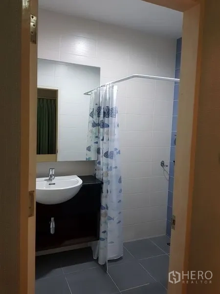 Townhouse for rent in Phra Khanong, Bangkok - Tiled bathroom with vanity sink, mirror and a shower area with curtain and handheld sprayer.