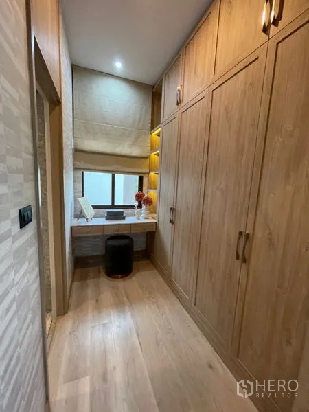 Detached House for sale in Bang Kapi, Bangkok - Walk-in closet corridor with floor-to-ceiling wooden wardrobes and a dressing desk.