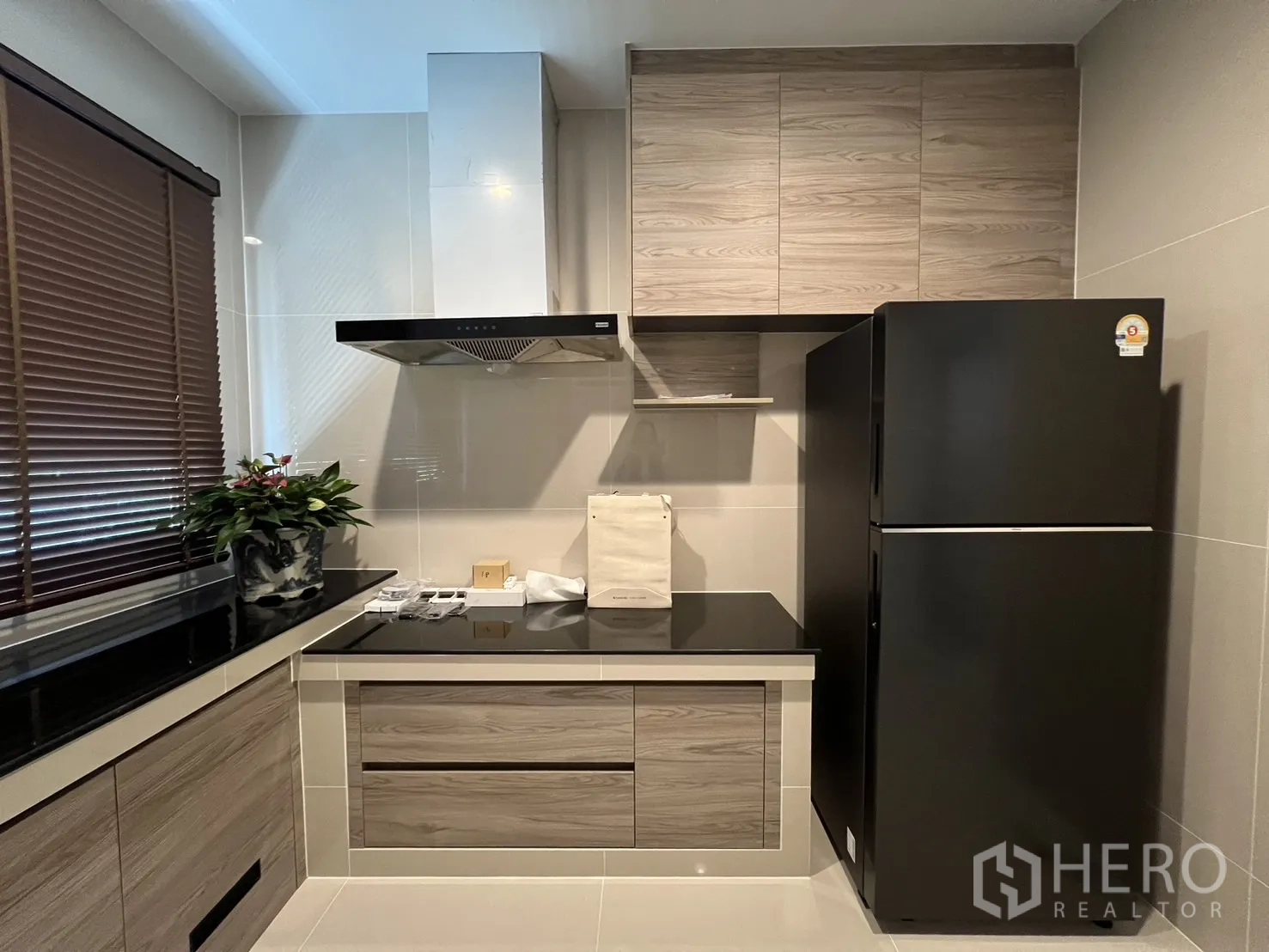 Detached House for rent or sale in Bang Kapi, Bangkok - Cooking area with electric hob, extractor and storage next to a refrigerator.