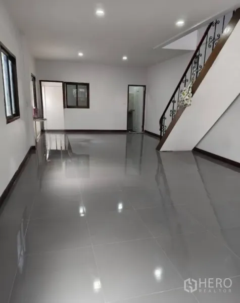 Townhouse for sale in Phra Khanong, Bangkok - Spacious ground-floor living area with glossy grey tiles, recessed lights and a staircase.