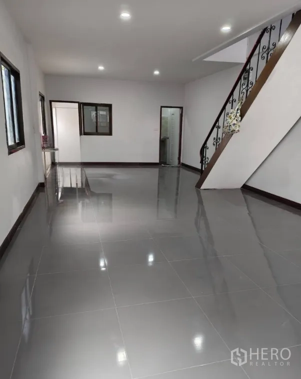 Townhouse for sale in Phra Khanong, Bangkok - Spacious ground-floor living area with glossy grey tiles, recessed lights and a staircase.