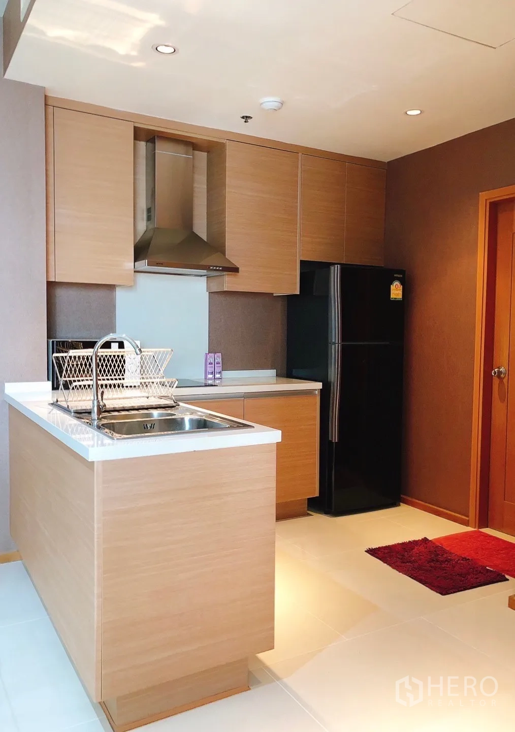 Condominium for rent in Khlong Toei, Bangkok - Kitchen view with black refrigerator, wood cabinets and bright tiled floor.