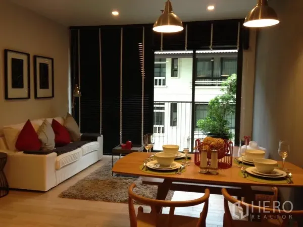 Condominium for rent in Watthana, Bangkok - Cozy living-dining room with sofa and rug, table set for four, and sliding doors to a small balcony.