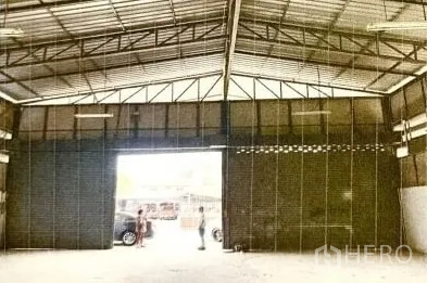 Warehouse for rent in Lat Phrao, Bangkok - High-clearance warehouse interior with steel truss roof and a large roller door opening to the driveway.