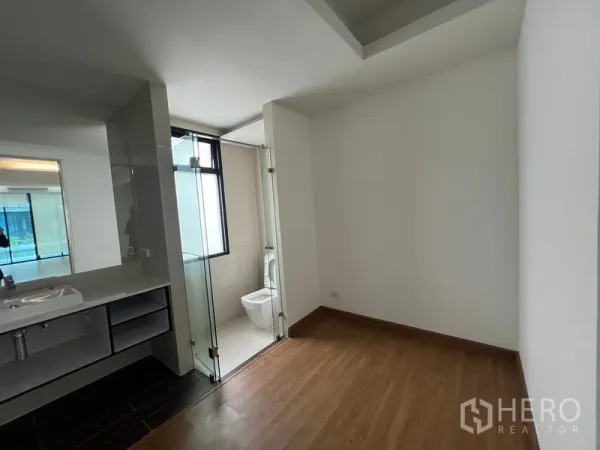 Townhouse for rent or sale in Khlong Toei, Bangkok - Bedroom with wood floors and an ensuite bathroom featuring a glass door and vanity.
