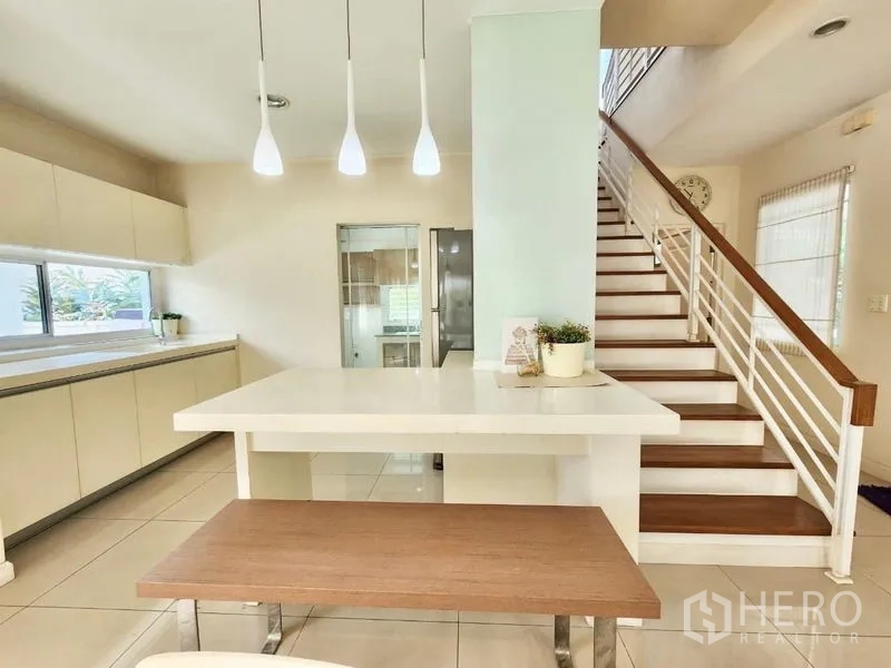 Detached House for rent in Prawet, Bangkok - Open-plan dining island with pendant lights beside the staircase leading to the kitchen.