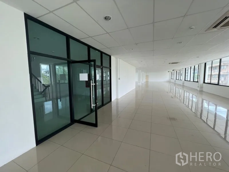 Office Space for rent - Open-plan office floor with glass-partition entrance, tiled floors, drop ceiling and long windows in Phra Khanong, Bangkok.