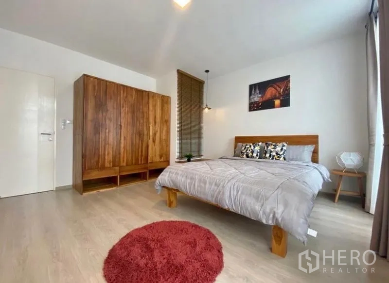 Townhouse for rent in Bang Phli, Samut Prakan - Large bedroom with wooden wardrobe, bedside tables and red rug on light wood flooring.