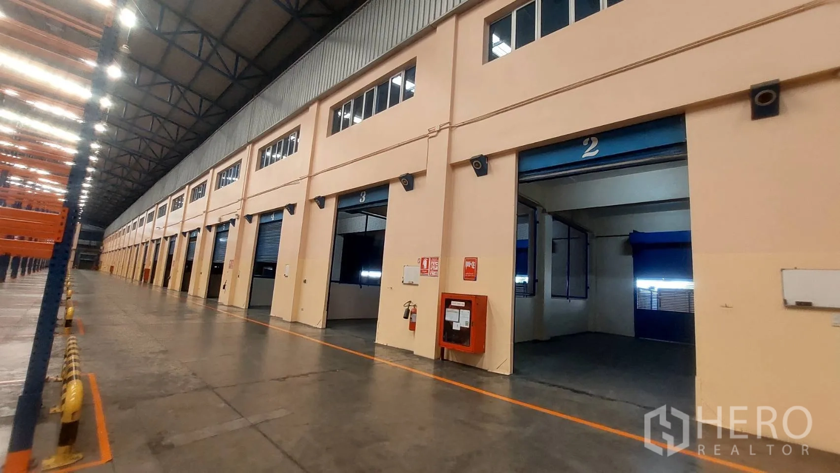Warehouse for rent in Mueang Pathum Thani, Pathum Thani - Row of loading bays with roller doors, fire equipment, and adjacent racking.