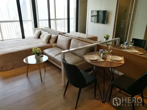 Condominium for sale in Khlong Toei, Bangkok - Dining nook for two beside the sofa and bed, next to wide windows and balcony with city view.