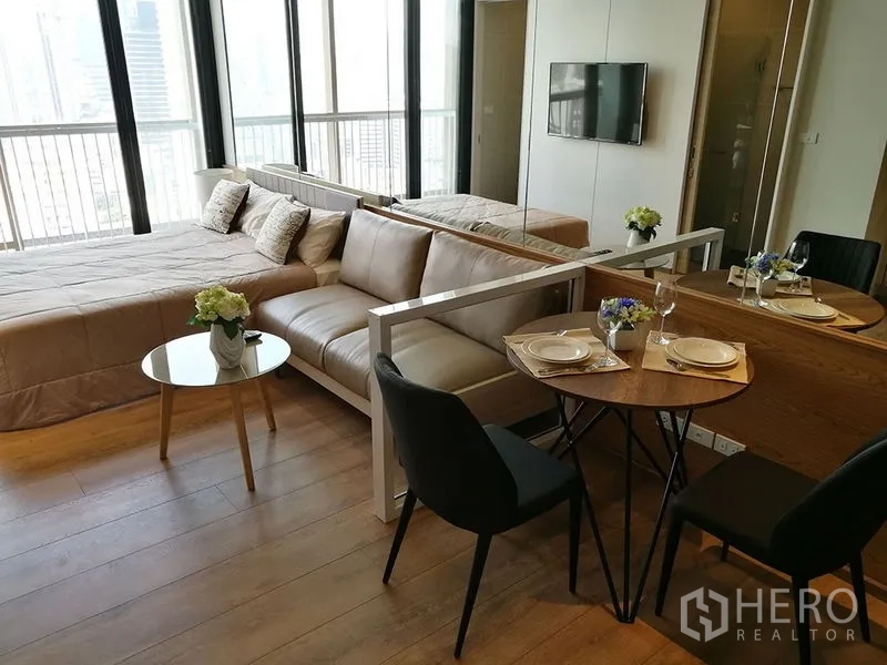 Condominium for sale in Khlong Toei, Bangkok - Dining nook for two beside the sofa and bed, next to wide windows and balcony with city view.